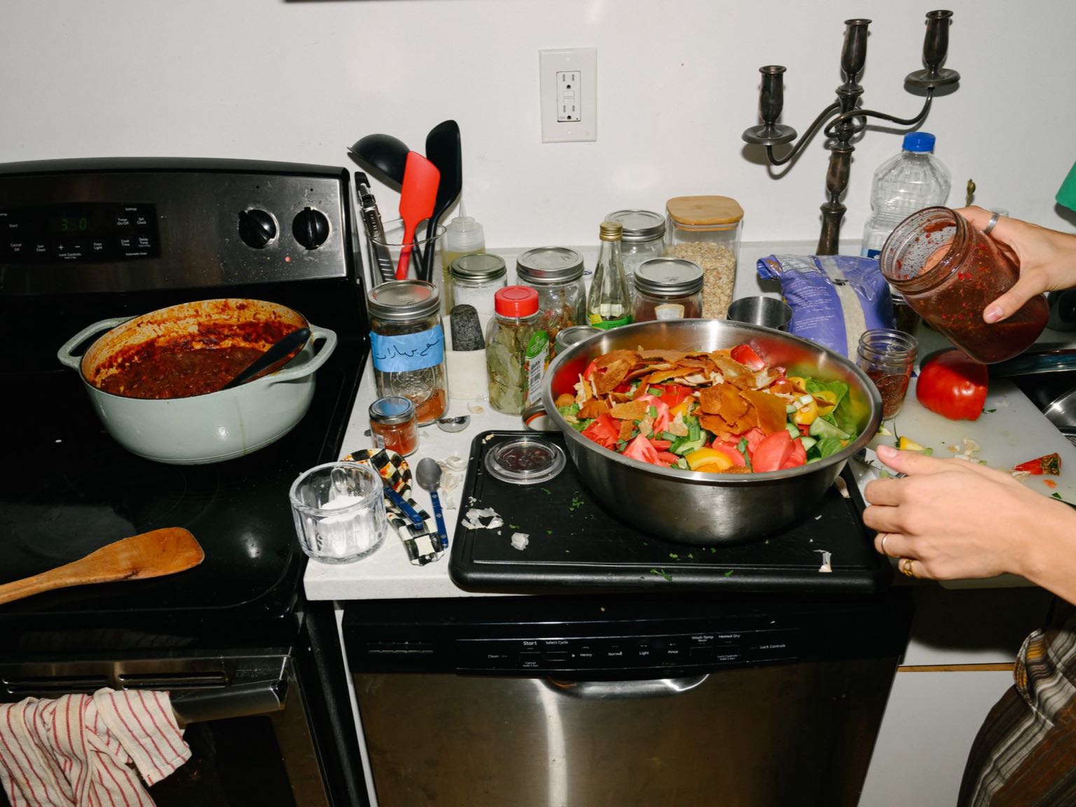 A cook spooning sauce over a bowl of fattoush beside a pot of stew on the stove