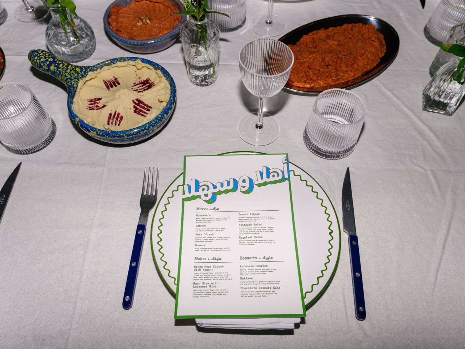 A place setting with a printed Lebanese dinner menu, hummus and muhammara